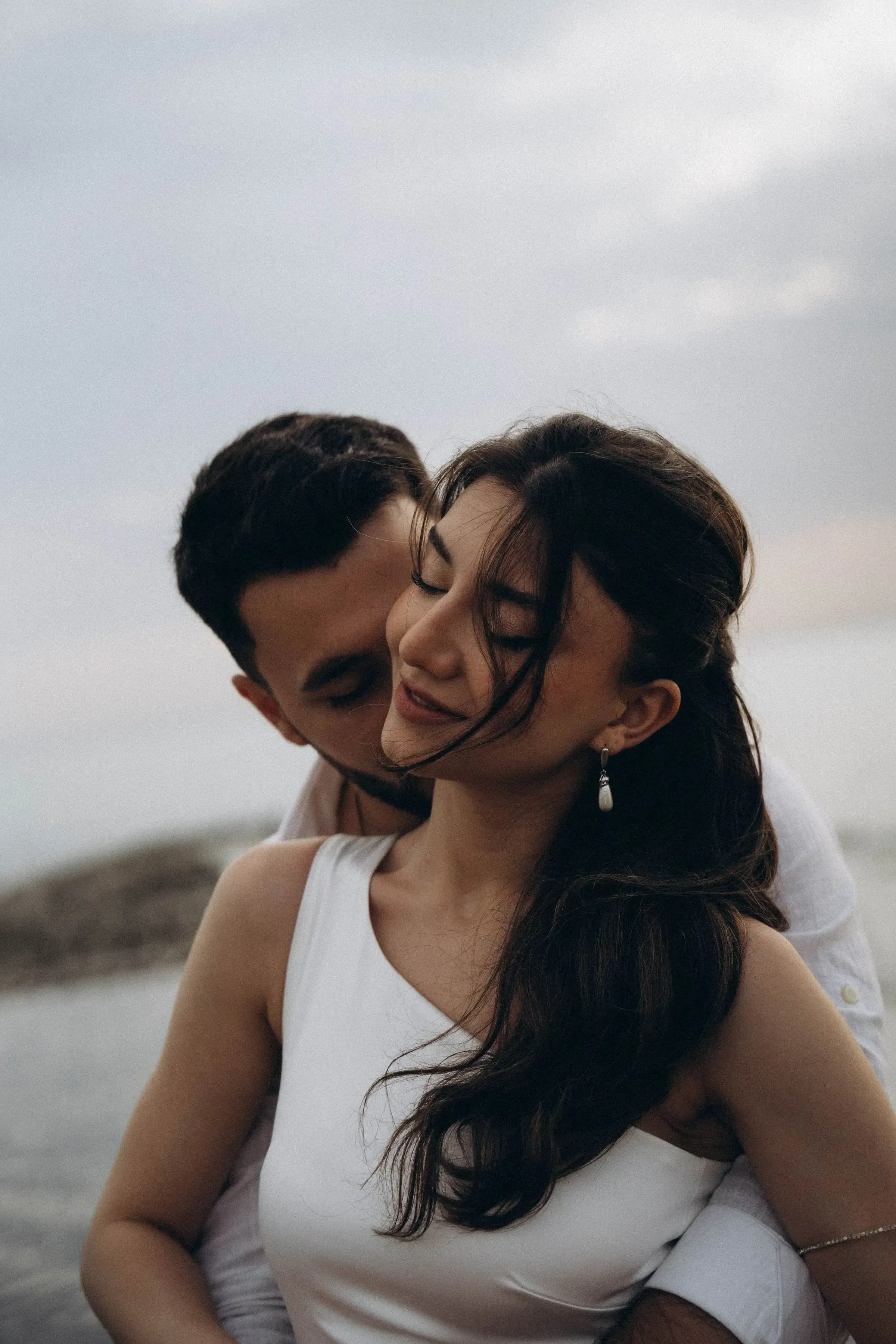 A newlywed couple shares an intimate moment by the beach at dawn.